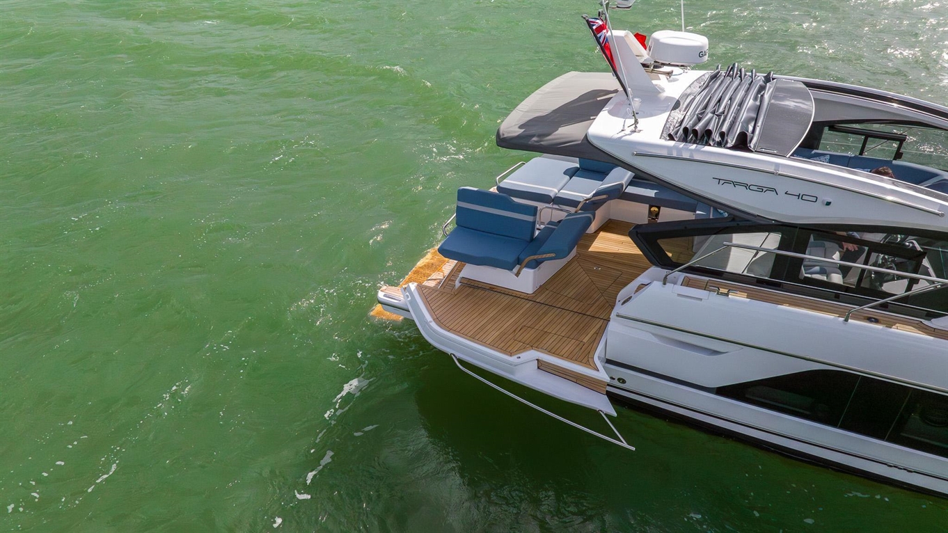Luxury Targa 40 yacht with blue seating and wooden deck on green waters, showcasing sleek design and elegance.